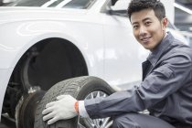 Chinese auto mechanic holding car wheel in workshop — Stock Photo