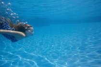 Pre-adolescent girl with fanning long hair swimming underwater in pool. — Stock Photo