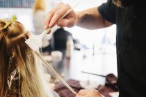 Male hairstylist using paintbrush for dyeing female blonde hair. — Stock Photo