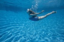 Pre-adolescent girl with fanning long hair swimming underwater in pool. — Stock Photo