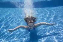 Pre-adolescent girl with fanning long hair swimming underwater in pool. — Stock Photo