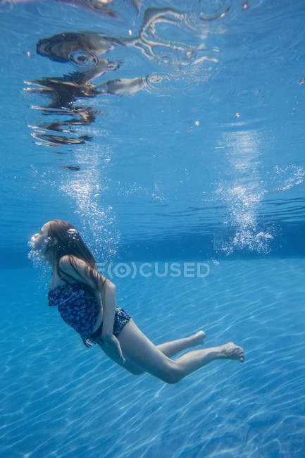 Pre-adolescent girl with fanning long hair swimming underwater in pool. — Stock Photo