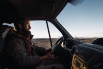 Smiling bearded man driving car on road in nature — Stock Photo