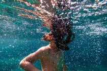 Anonymous boy in diving mask snorkeling in bubbling water of blue sea — Stock Photo