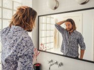 Handsome young man checking hairstyle in mirror reflection — Stock Photo