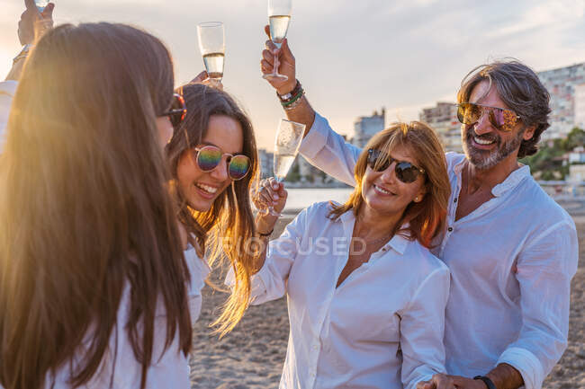 Allegro genitori maturi e giovani figlie clinking bicchieri di vino e ridere mentre si celebra riunione di famiglia in serata sul resort — Foto stock