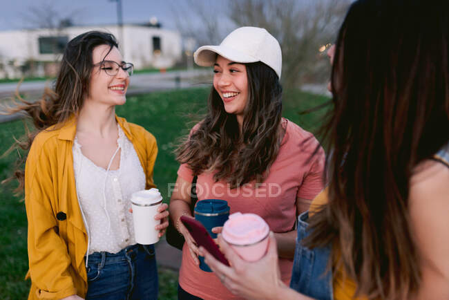 Crop content migliori amiche con bevande calde in bicchieri parlando mentre si guardano in città — Foto stock