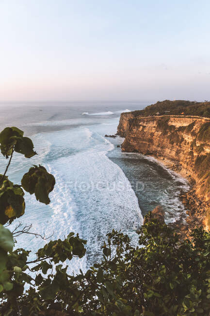 Ruvida scogliera rocciosa bagnata da un mare ondulato e schiumoso sotto un cielo blu senza nuvole in una natura panoramica — Foto stock