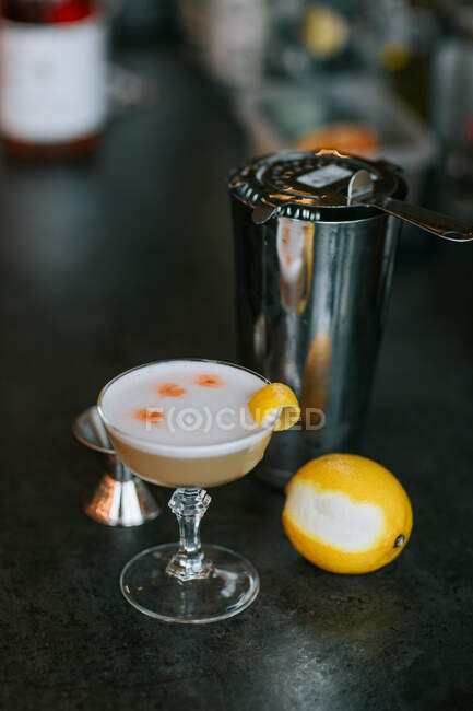 High angle of transparent glass with cold alcoholic cocktail pisco sour with lemon zest placed near shaker — Stock Photo