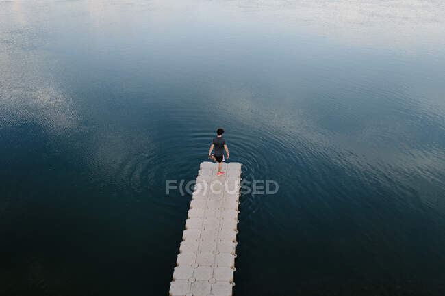 Dall'alto vista remota di maschio in piedi sul bordo del molo vicino al lago calmo — Foto stock