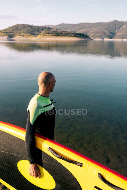 Vista laterale del surfista maschio irriconoscibile ritagliato in muta con tavola SUP gialla e pagaia in acqua di mare — Foto stock