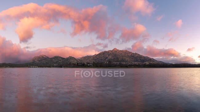 Acqua di mare che scorre contro la riva con ruvida montagna rocciosa contro il colorato cielo blu con nuvole bianche in natura al tramonto — Foto stock