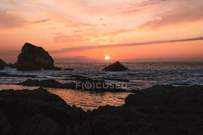 Incredibile scenario tranquillo del tramonto sul mare ondulato increspato con rocce sotto cielo nuvoloso colorato in estate sera a Liencres Cantabria Spagna — Foto stock