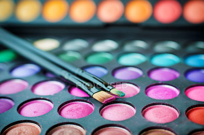 Close-up of multi-colored eyeshadow palette and make up brushes — Stock Photo