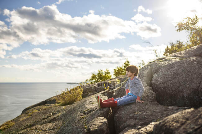 Boy sitting on rocks by a lake, Lake Superior Provincial Park, Stati Uniti — Foto stock