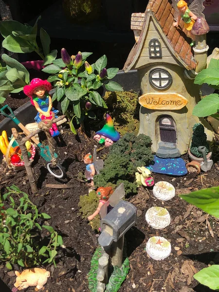 Fairy garden in a pot with house and creatures like pixies, fairies and pigs hanging out outside in a mini garden