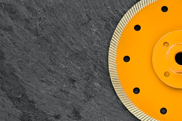 Diamond cut-off wheel with thin cutting segments for cutting stone and granite, yellow circle body with threaded nut, against dark gray granite background, Copy space, close-up.