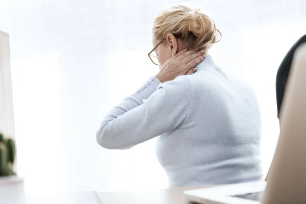 Woman at workplace sitting and holding sore neck.