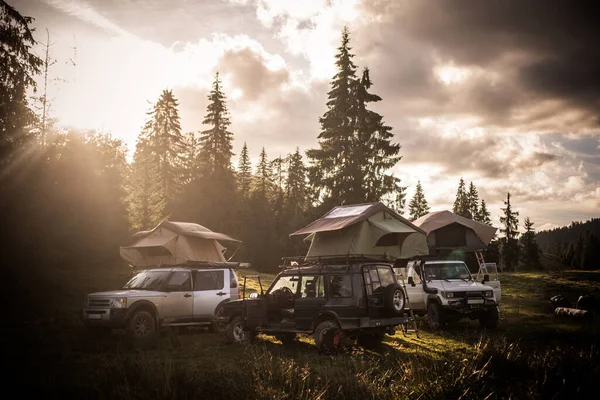 Some off road cars with rooftop tents in a forest, at sunset.