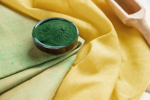 Green spirulina powder on a yellow  napkin .  Organic green spirulina powder on yellow background. Super foods.  Food supplement source of vitamin protein and beta carotene.   Immunity support .