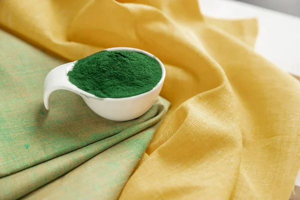 Green spirulina powder on a yellow  napkin .  Organic green spirulina powder on yellow background. Super foods.  Food supplement source of vitamin protein and beta carotene.   Immunity support .