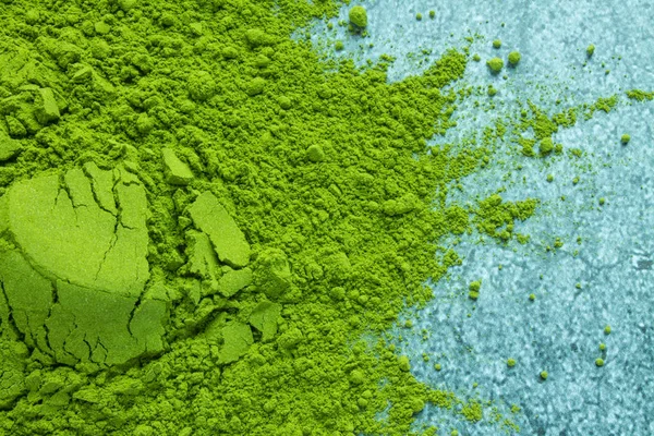 Scattered green powder of traditional Japanese matcha tea in close-up on a grey textural background with copy space