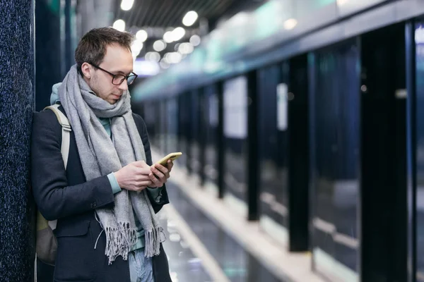 Hipster chatting and sending messages using his smartphone and misses all trains. Copy space. Social networks are delaying and take a lot of time. Mobile phone and internet addiction concept.