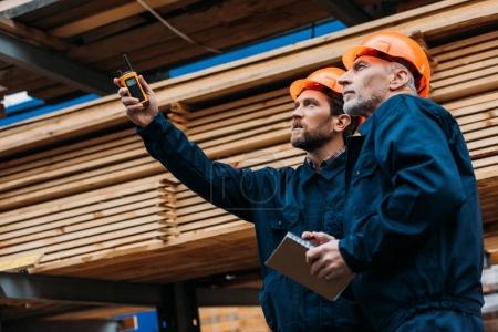 Foto de Constructores en cascos apuntando con walkie talkie en la construcción - Imagen libre de derechos