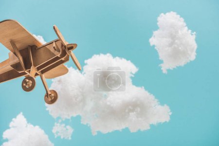 Foto de Avión de juguete de madera volando entre nubes esponjosas blancas hechas de algodón aislado en azul - Imagen libre de derechos