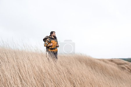 Foto de Joven barbudo con mochila de pie y mirando hacia el campo - Imagen libre de derechos