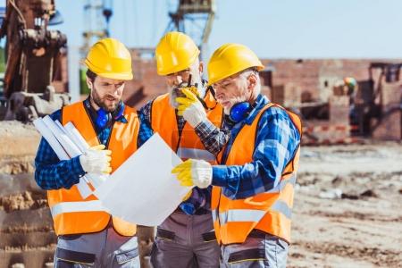 Foto de Tres trabajadores examinan planos de construcción en obra - Imagen libre de derechos