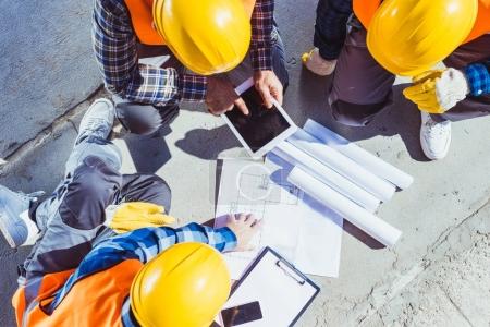 Foto de Tres trabajadores de la construcción sentados en concreto y discutiendo planes de construcción - Imagen libre de derechos