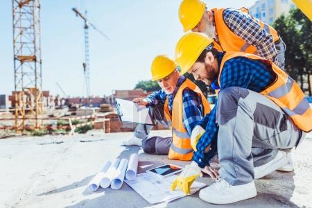 Foto de Trabajadores de la construcción en uniforme sentados en concreto en el sitio de construcción, discutiendo planes de construcción - Imagen libre de derechos