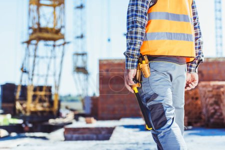 Foto de Recortado tiro del constructor en chaleco reflectante de pie en el sitio de construcción - Imagen libre de derechos