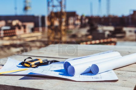 Foto de Rollos de papel con planos de construcción y radio portátil sobre superficie de madera en obra - Imagen libre de derechos