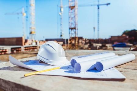 Foto de Rollos de papel con planos de construcción y hardhat sobre superficie de madera en obra - Imagen libre de derechos