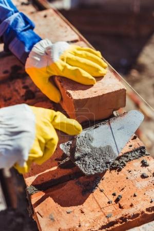 Foto de Tiro recortado del trabajador de la construcción en guantes protectores que ponen ladrillos usando espátula - Imagen libre de derechos