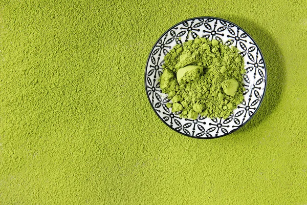 Green tea matcha powder in ceramic bowl over powdering matcha as background. Flat lay, copy space