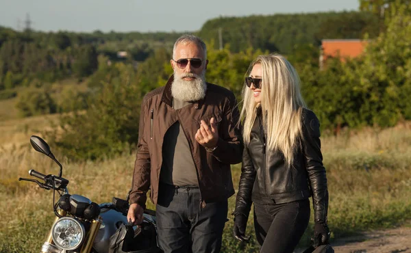 Two old and young happy people wearing leather costumes against motorbike.