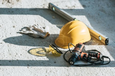 Foto de Vista de cerca de hardhat, nivel de espíritu, taladro y guantes de protección con googles en el sitio de construcción - Imagen libre de derechos