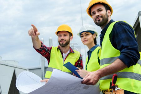 Foto de Ingenieros profesionales en chalecos de seguridad y sombreros de trabajo con planos y mostrando la construcción - Imagen libre de derechos