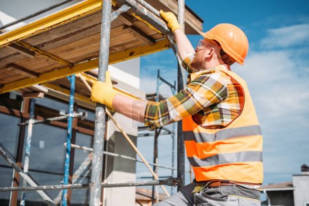 Foto de Hermoso constructor escalando en andamios en el sitio de construcción - Imagen libre de derechos