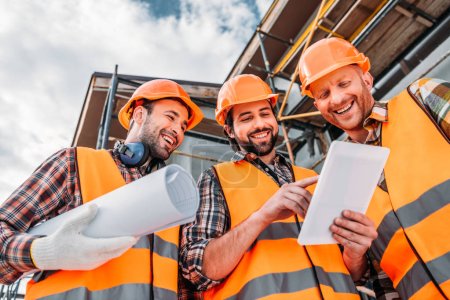 Foto de Vista inferior del grupo de constructores con plano y tableta en el sitio de construcción - Imagen libre de derechos