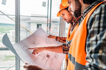 Foto de Constructores reflexivos que trabajan con el plan en el sitio de construcción - Imagen libre de derechos