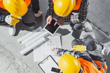 Foto de Vista superior de tres trabajadores de la construcción sentados en concreto y discutiendo planes de construcción - Imagen libre de derechos