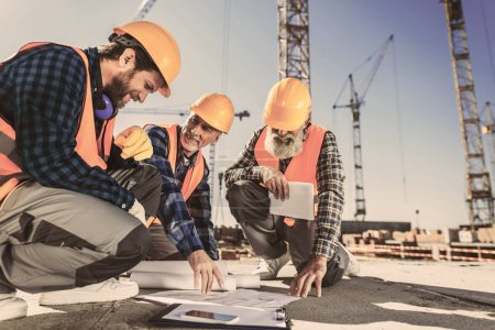 Foto de Trabajadores de la construcción sentados en concreto en el sitio de construcción y mirando los planos de construcción - Imagen libre de derechos