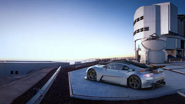 Silver sports car parked on a rooftop with a modern industrial building in the background.