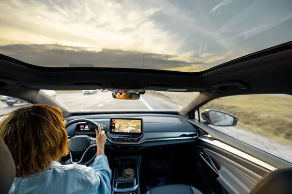 Woman drives car with panoramic rooftop on sunset. Interior view from a backside. Modern cars and travel concept