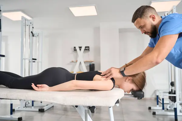 Massage therapist at workplace straightens back of a young female, a woman lies on her stomach on a massage table