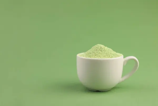 in a white cup there is a light green powder. healthy matcha tea. light green background